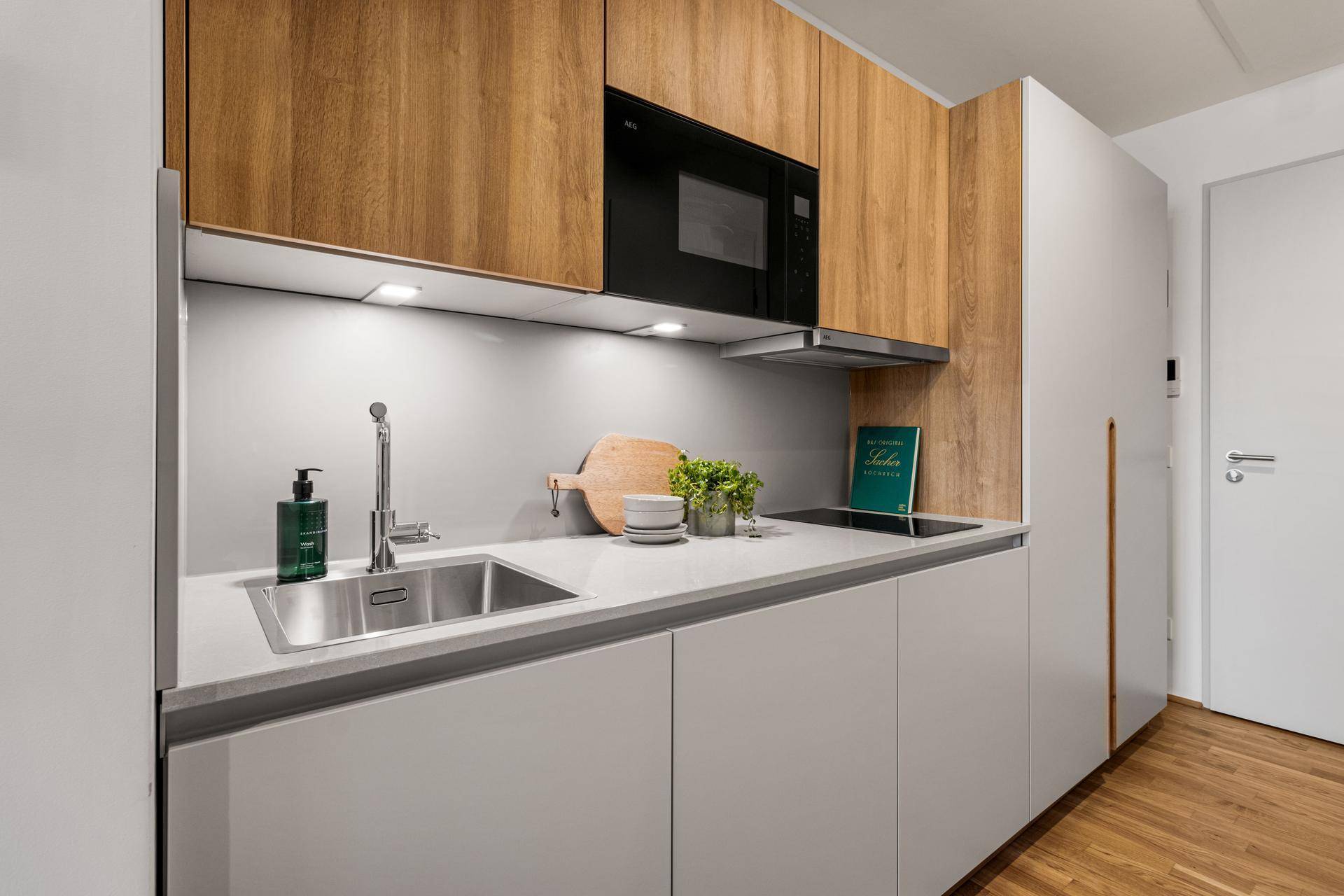 Moderne Küchenzeile mit Holzakzenten, Induktionskochfeld, Mikrowelle und integriertem Kühlschrank.