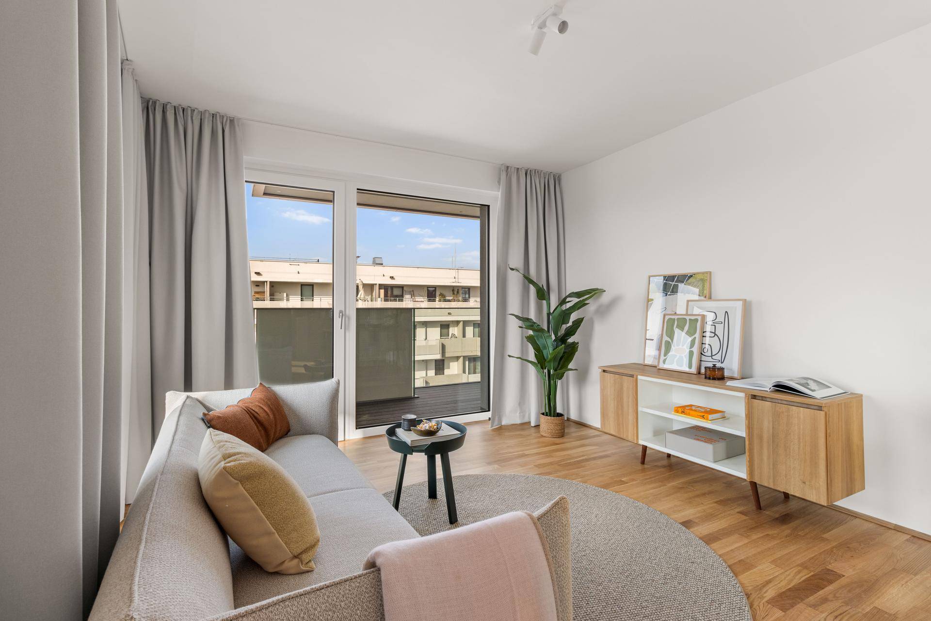 Gemütliches Wohnzimmer mit Sofa, Medienkonsole und großen Fenstern zum Balkon.