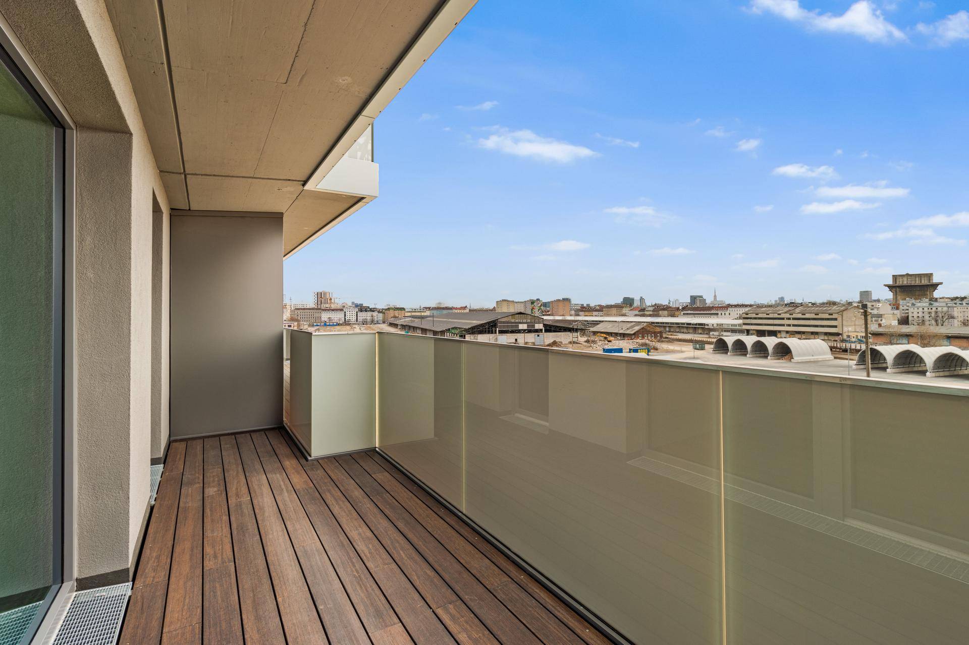 Geräumiger Balkon mit Holzboden und Glasgeländer, bietet einen weiten Blick über die Stadtlandschaft.