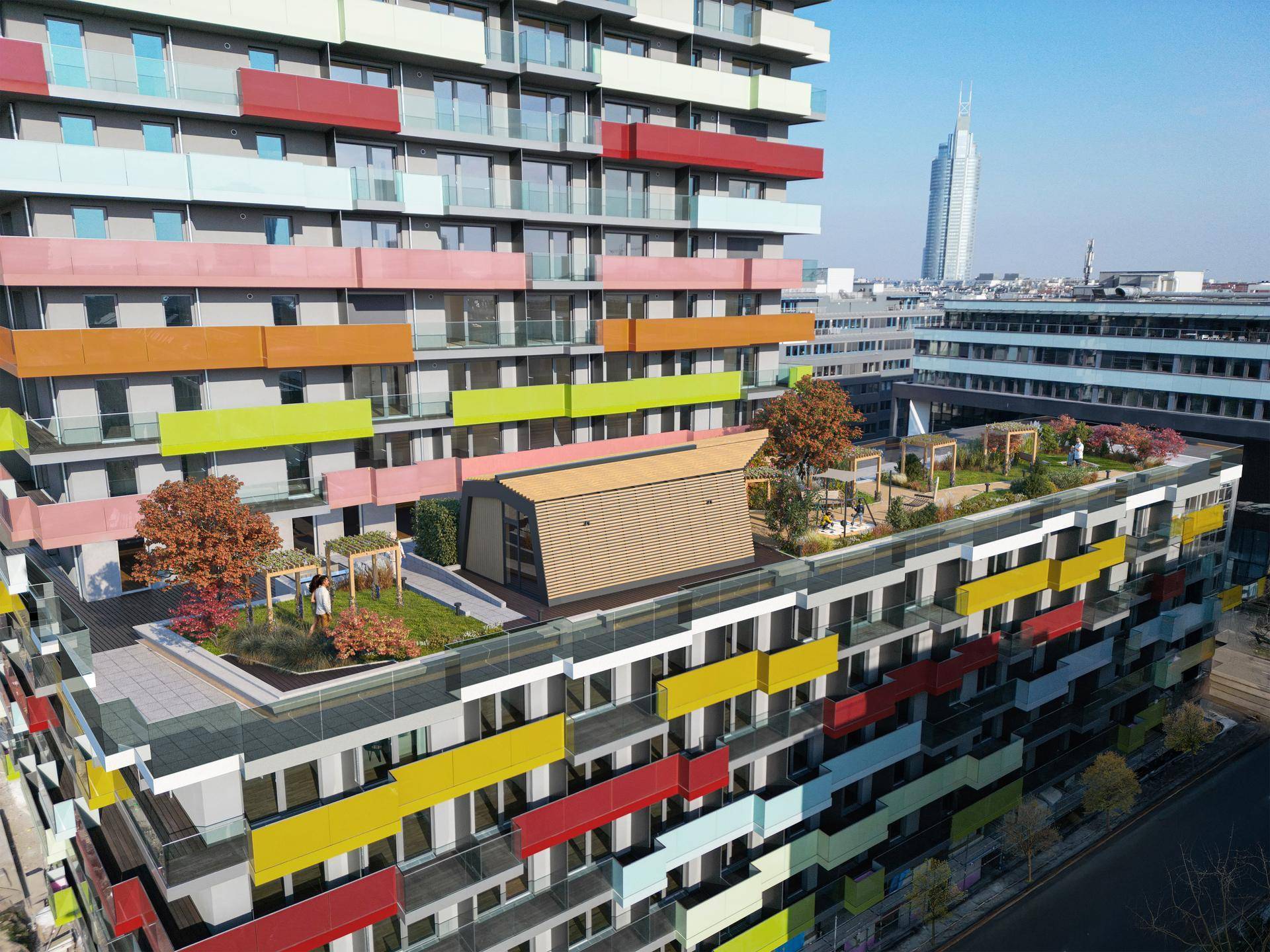 Moderne Wohnanlage mit farbigen Balkonen und begrüntem Dachgarten in einer urbanen Umgebung.
