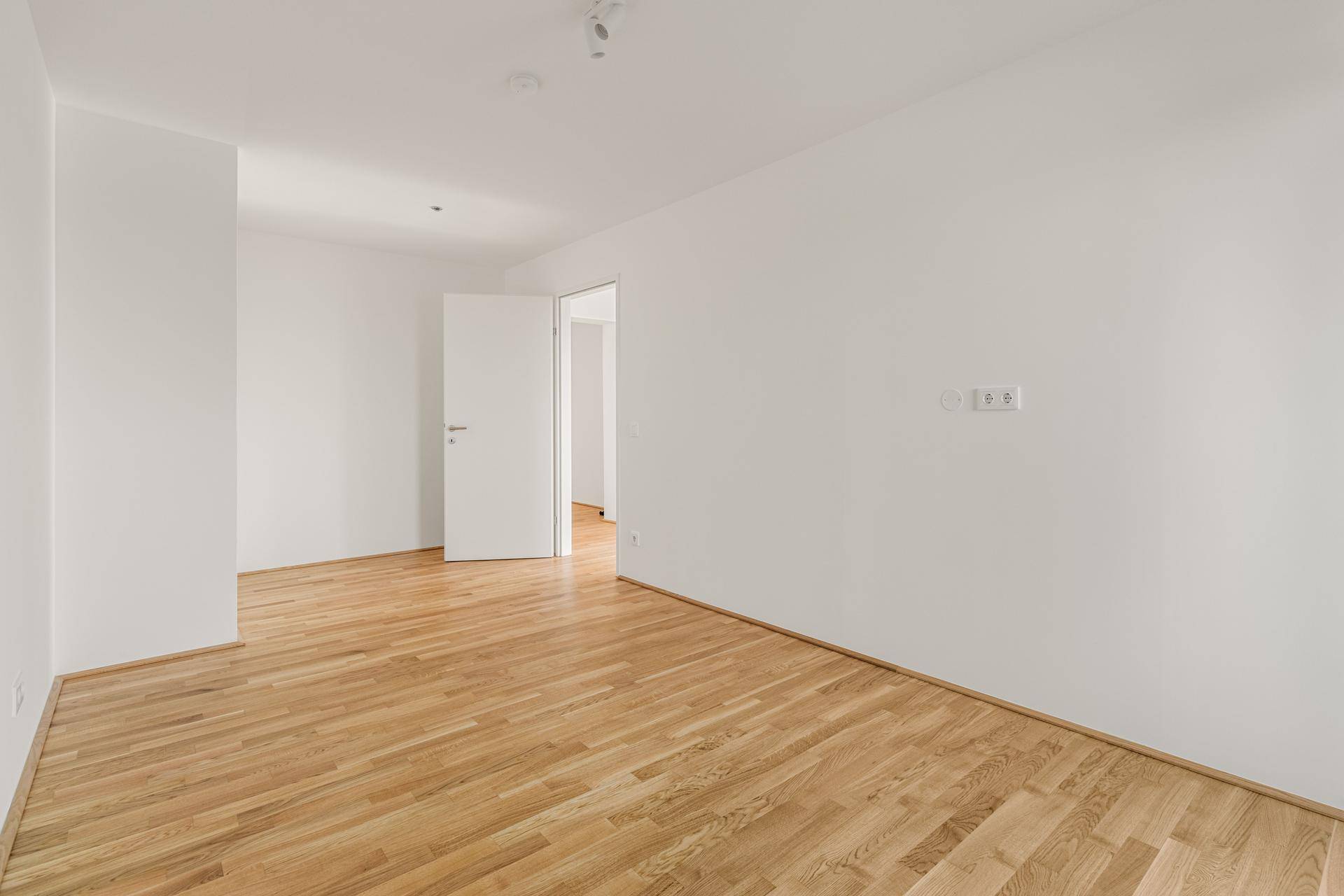 Leeres Zimmer mit hellem Parkettboden und weißen Wänden, bereit zur individuellen Gestaltung.
