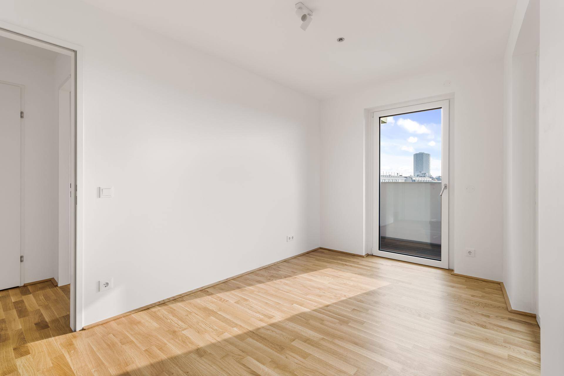 Freundliches Zimmer mit Parkett und Balkonzugang, bietet einen schönen Blick auf die Stadtlandschaft.