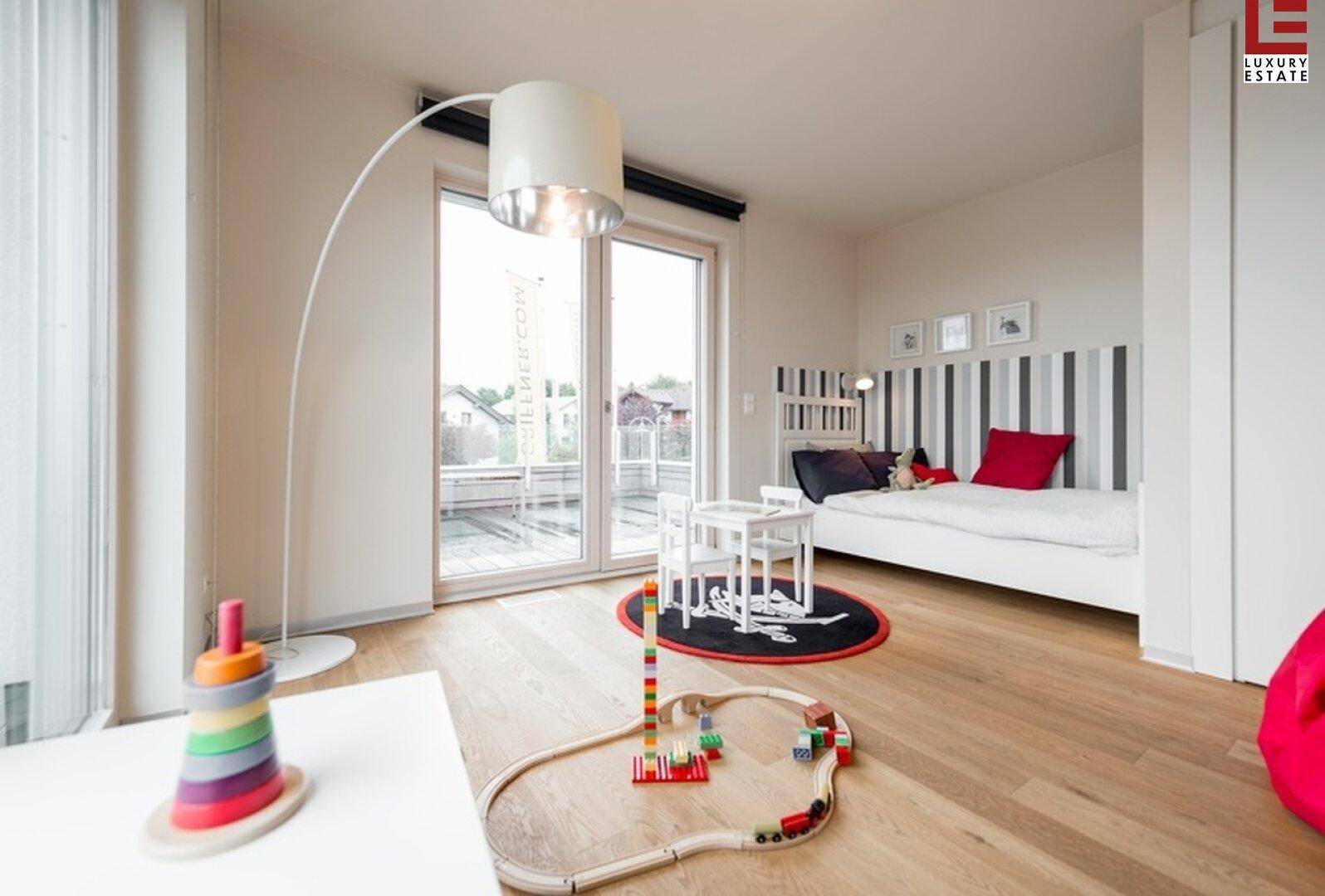 Helles Kinderzimmer mit Holzboden, Spielzeug und Zugang zu einem Balkon.