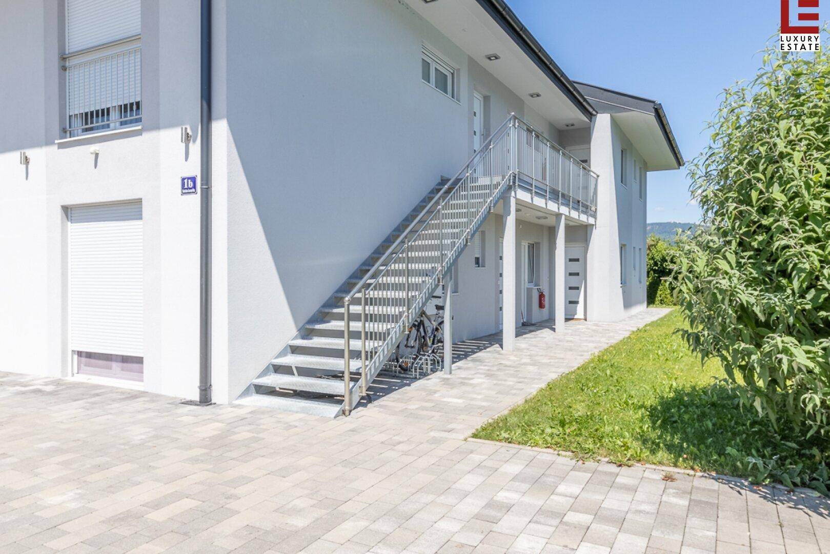 Seitenansicht des Gebäudes mit Außentreppe, gepflastertem Weg und Rasenfläche.