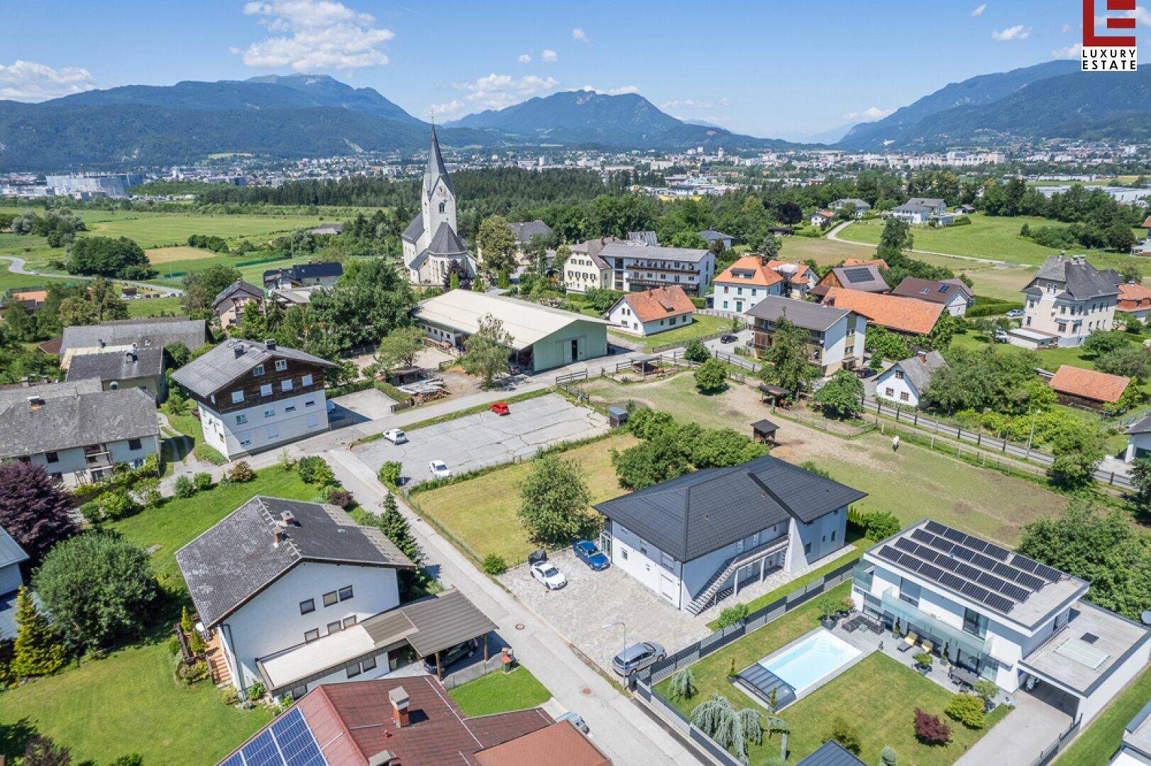 Panoramablick aus der Luft auf eine ländliche Siedlung mit Kirche und Bergkulisse.