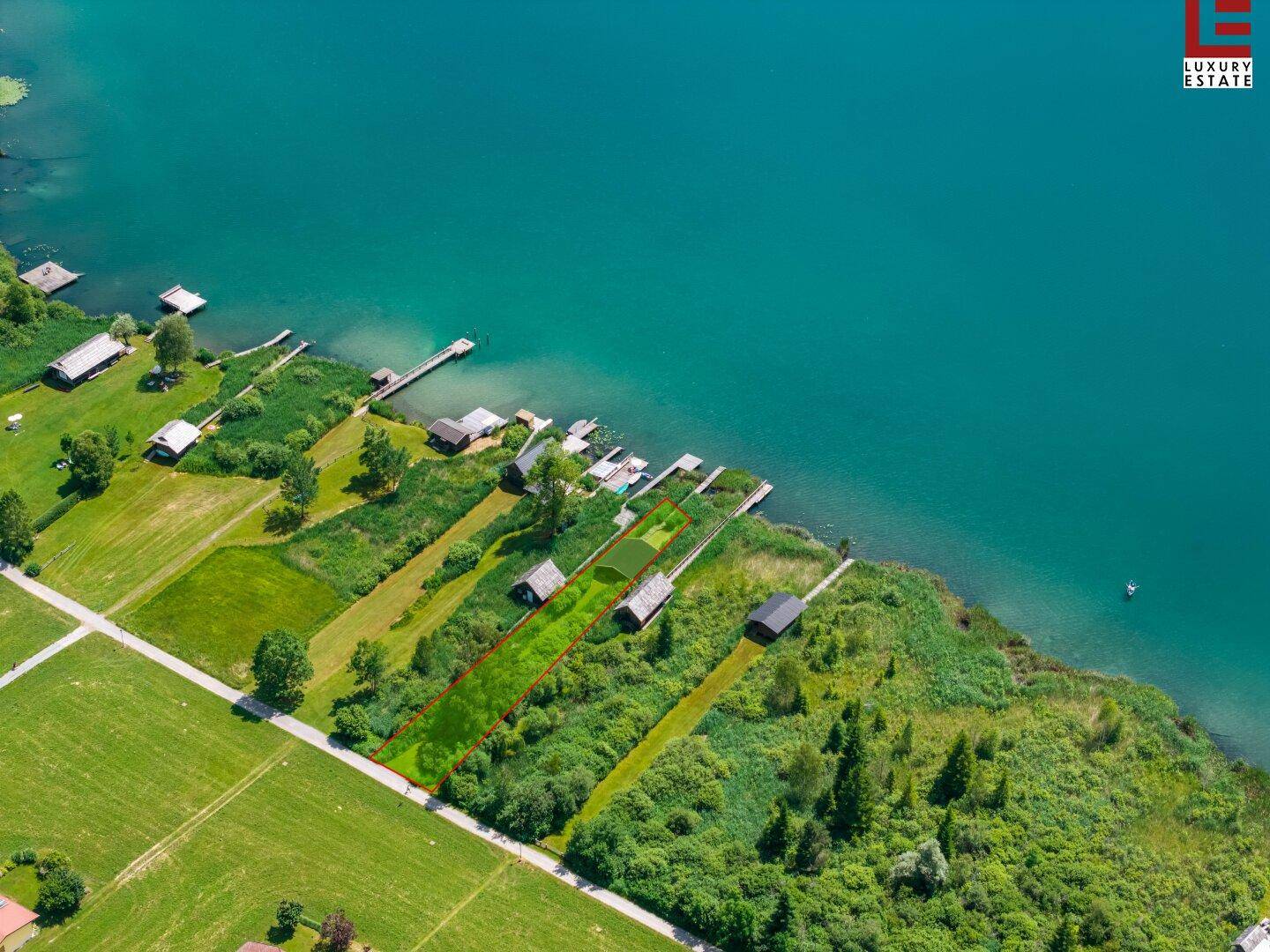 Luftaufnahme eines Seeufergrundstücks mit markierter Fläche, kleinen Hütten und privaten Stegen am Wasser.