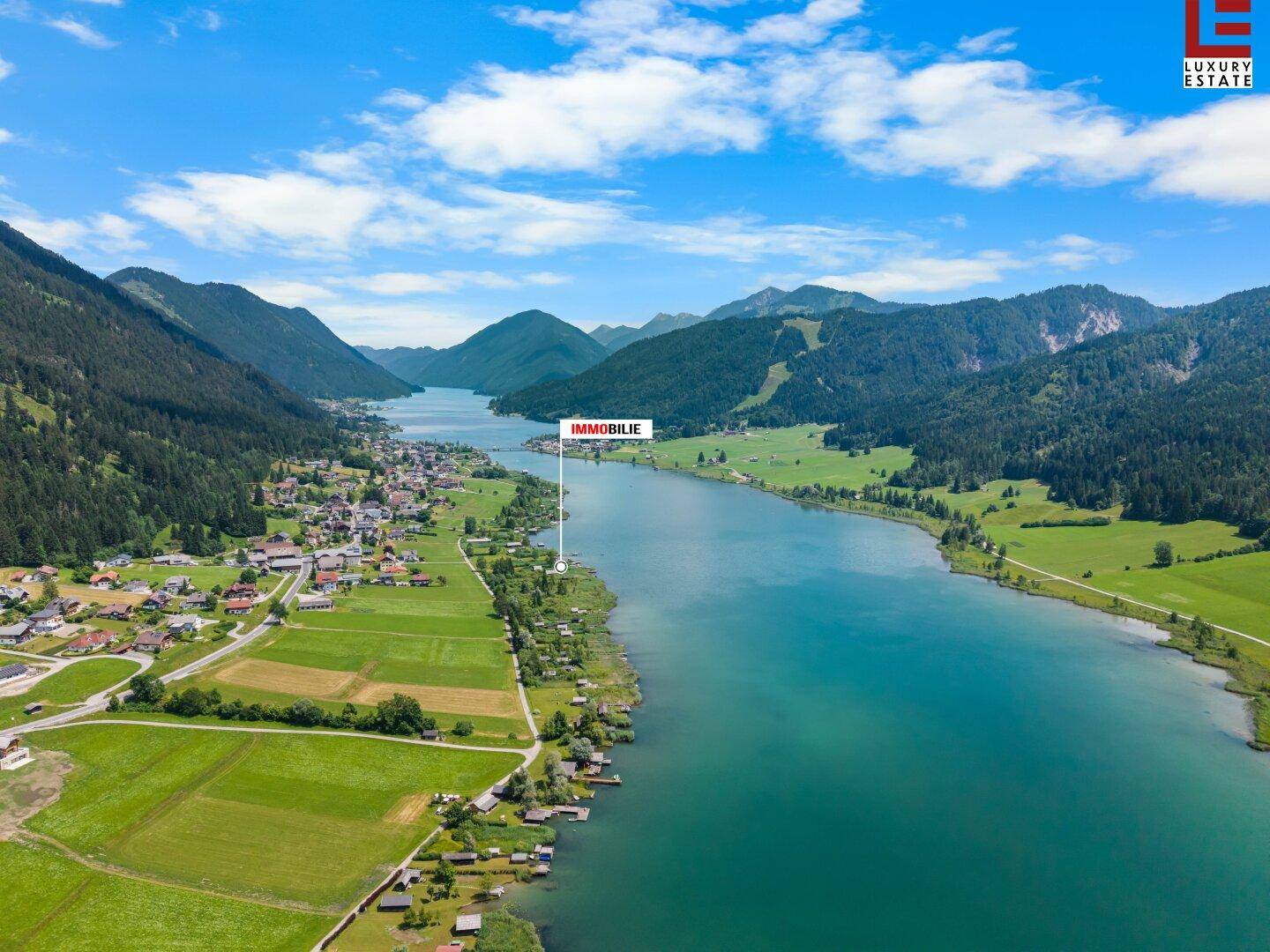 Panoramische Luftaufnahme des Sees und der umliegenden Landschaft mit markiertem Immobilienstandort.