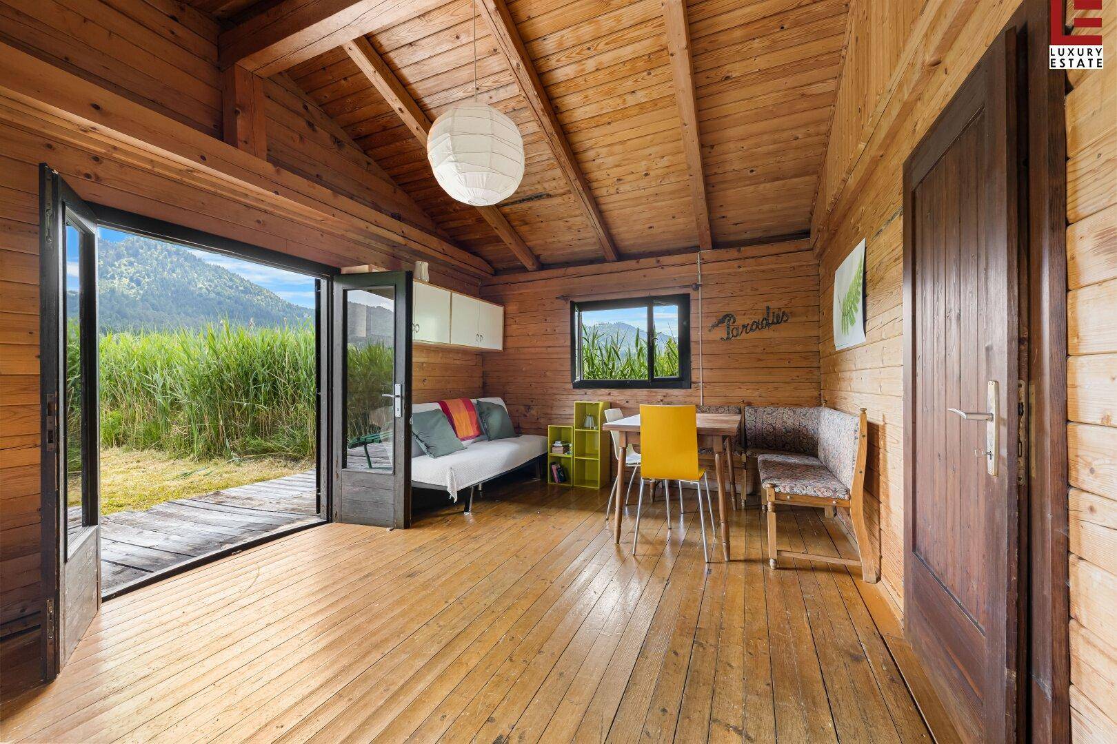 Gemütlicher Innenraum einer Holzhütte mit Holzböden und -wänden, großen Türen und Blick ins Grüne.