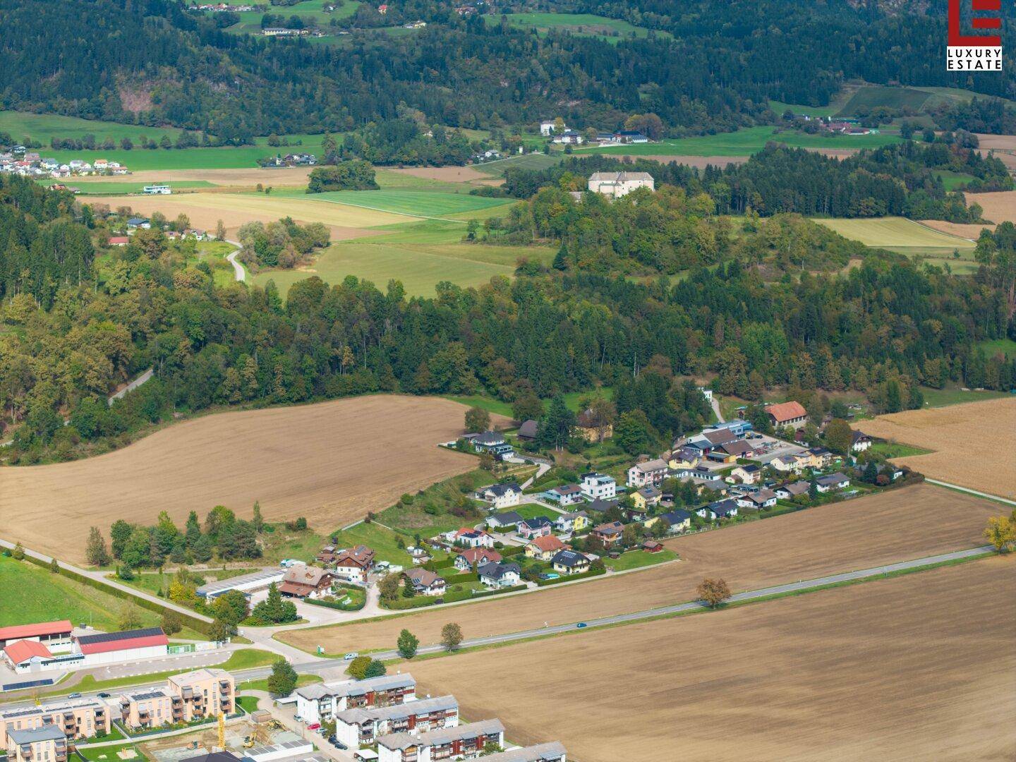 Weitläufige Luftaufnahme der ländlichen Umgebung mit Häusern, Feldern und bewaldeten Hügeln.