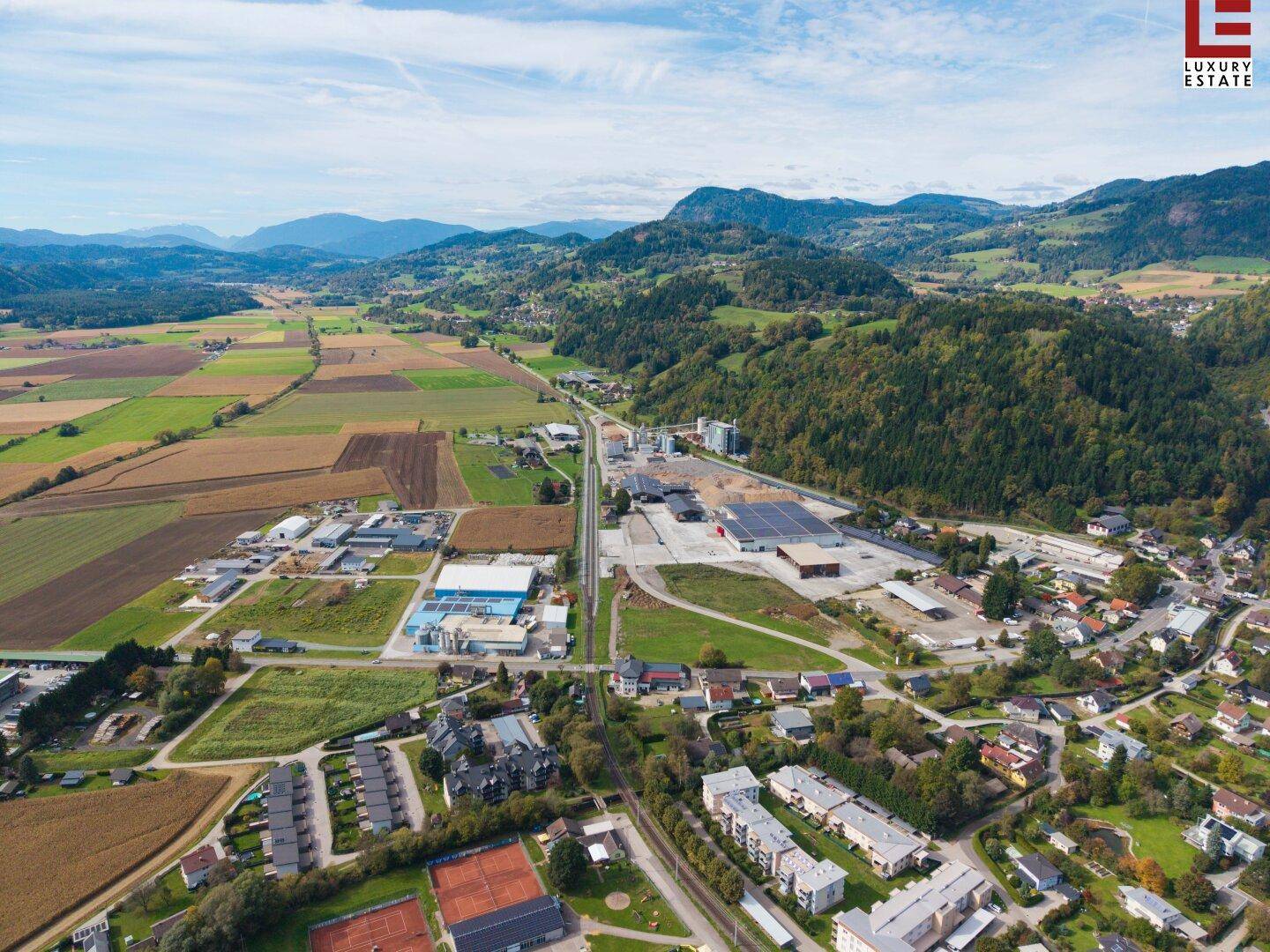 Luftaufnahme einer Mischung aus Wohn- und Industriegebiet mit Sportanlagen und Bergen im Hintergrund.