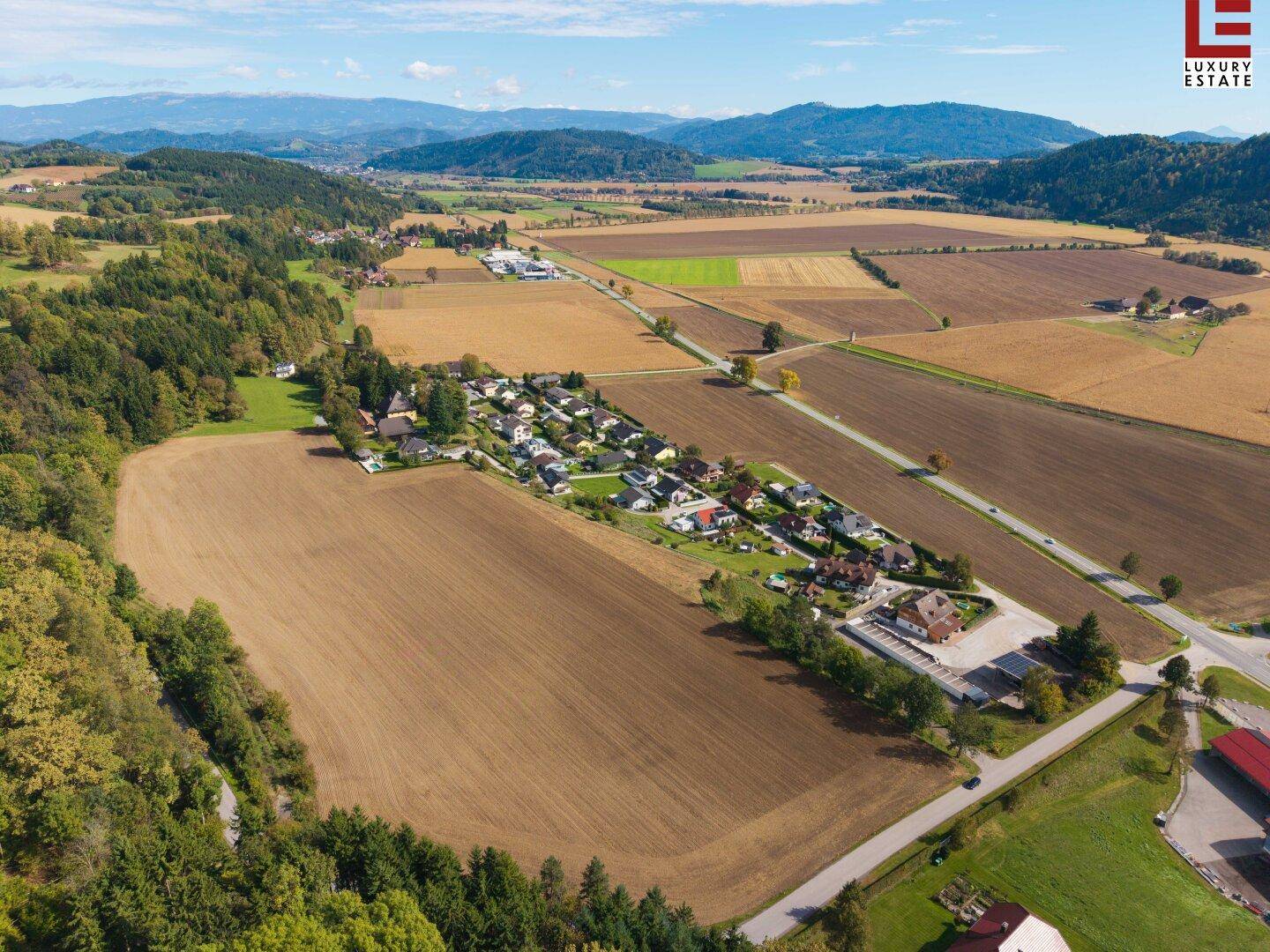 Panoramablick aus der Luft auf eine Wohnsiedlung, umgeben von Ackerland und einer weiten Landschaft.