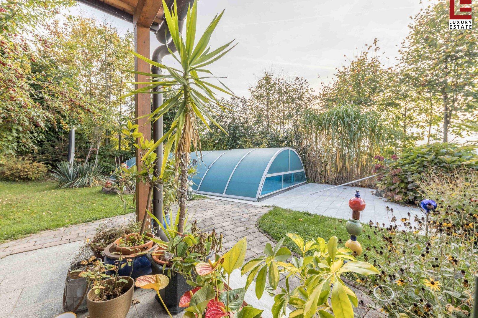 Gepflegter Gartenbereich mit überdachtem Pool, gepflasterter Terrasse und üppiger Bepflanzung.