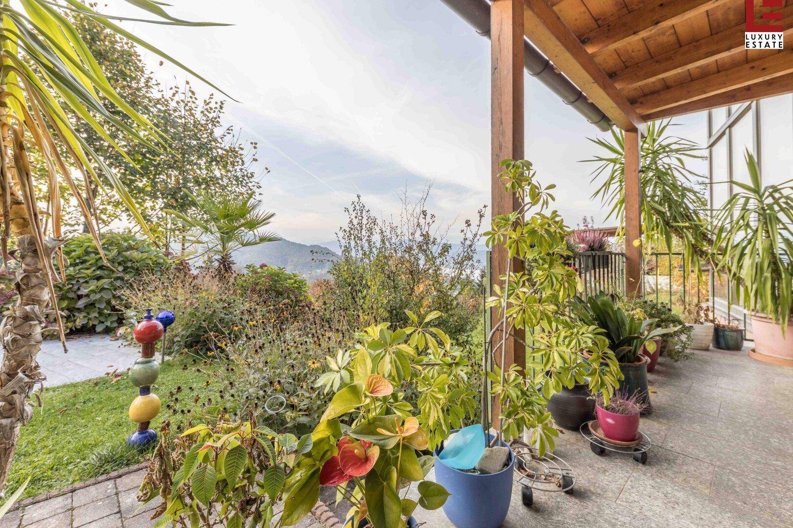 Blick von der überdachten Terrasse in den grünen Garten mit Pflanzen und weitem Ausblick.