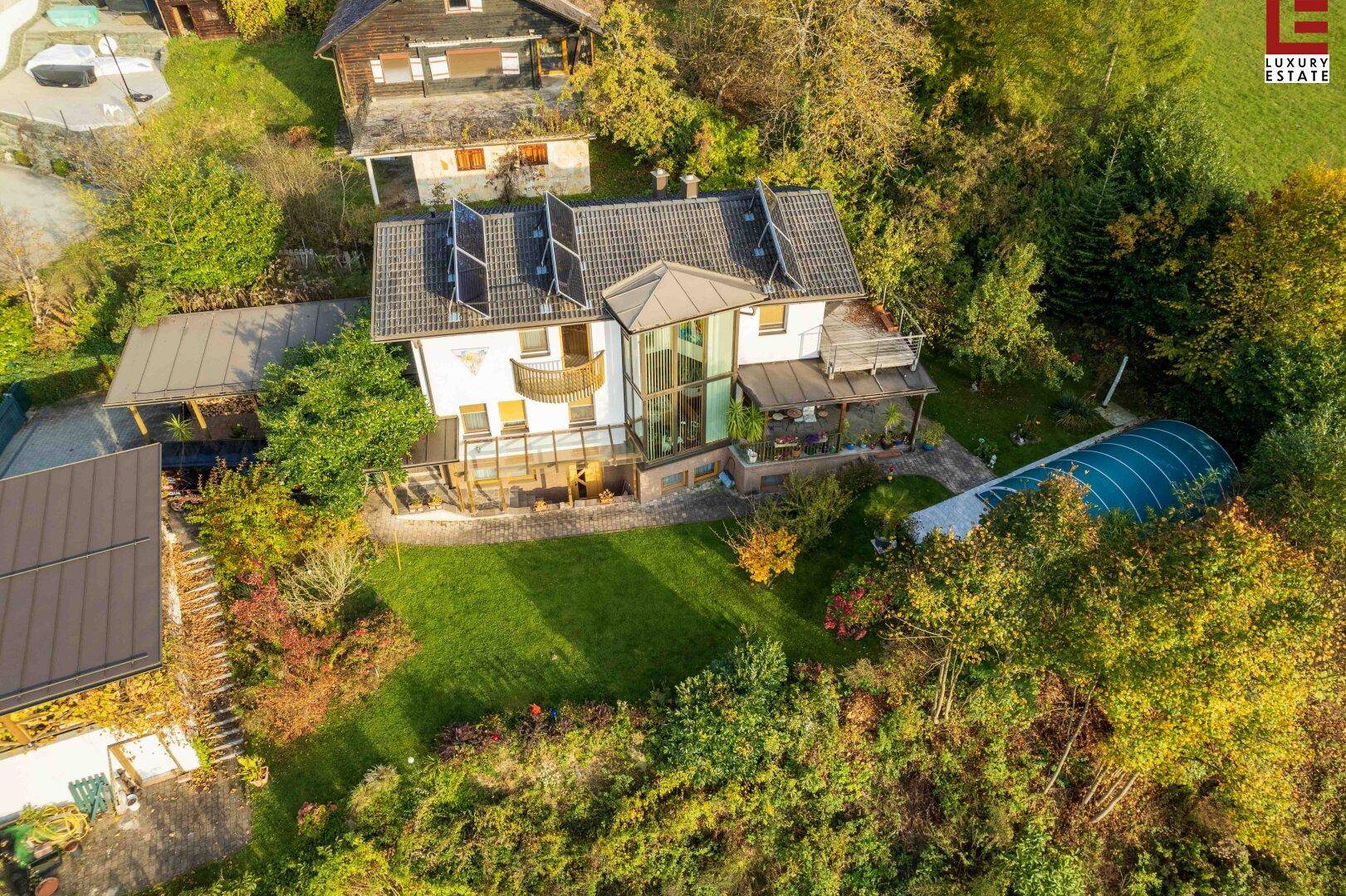 Luftaufnahme des Hauses mit Garten, überdachtem Pool und umliegender Natur.