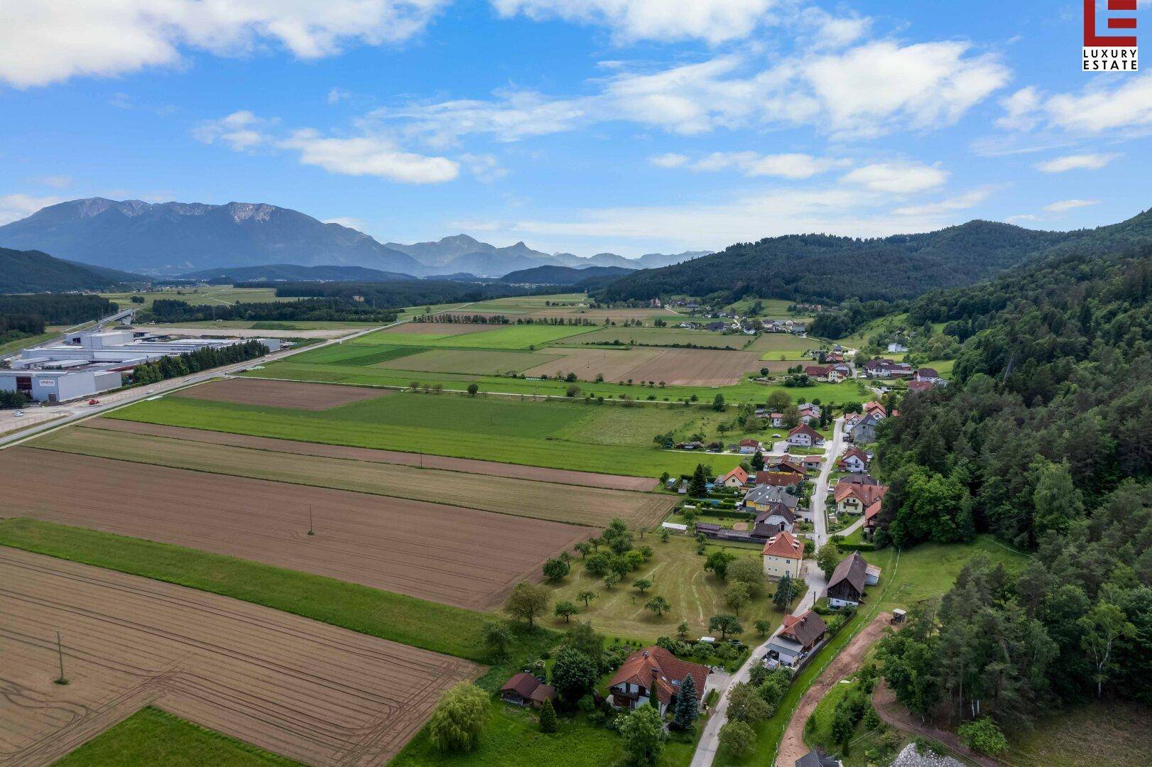 Weitläufige Luftaufnahme einer ländlichen Region mit Feldern, Wäldern und einer Bergkette am Horizont.