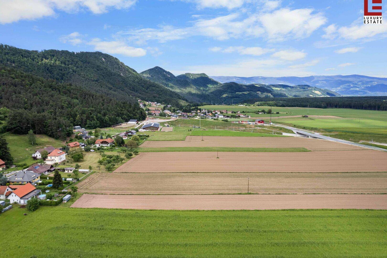 Weitläufige Luftaufnahme einer ländlichen Region mit Feldern, Wäldern, Bergen und einer Straße.