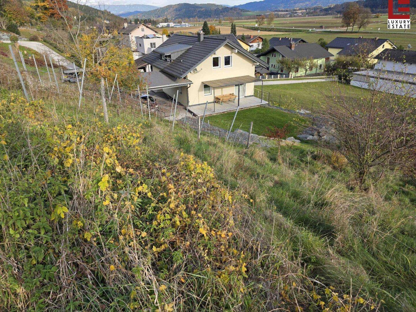 Hügeliges, naturbelassenes Gelände mit Blick auf ein Wohnhaus und die umliegende Landschaft.