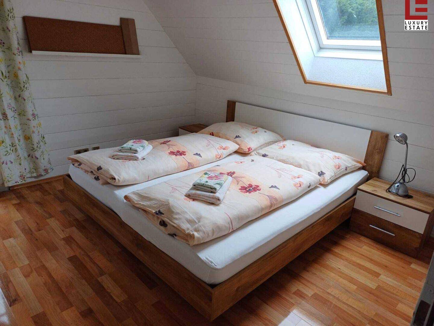 Helles Schlafzimmer mit Holzbett, Holzboden und Dachfenster für viel Tageslicht.