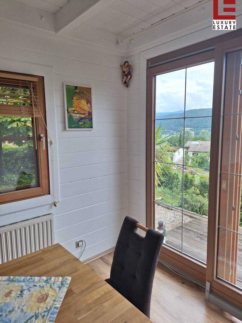 Essbereich mit Holztisch und großen Fenstern, die einen weiten Blick ins Grüne bieten.