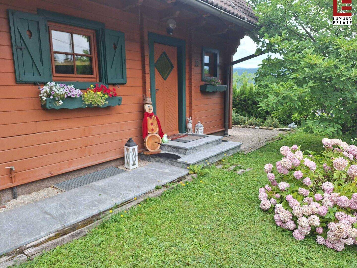 Eingangsbereich des Holzhauses mit Steinstufen, Blumenkästen und blühenden Hortensien.