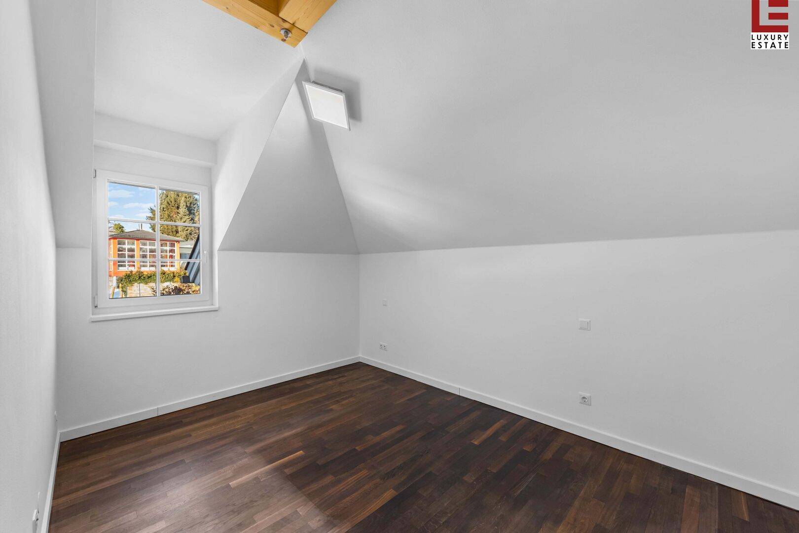 Gemütliches Schlafzimmer im Dachgeschoss mit Holzboden und einem Fenster mit Blick ins Grüne.