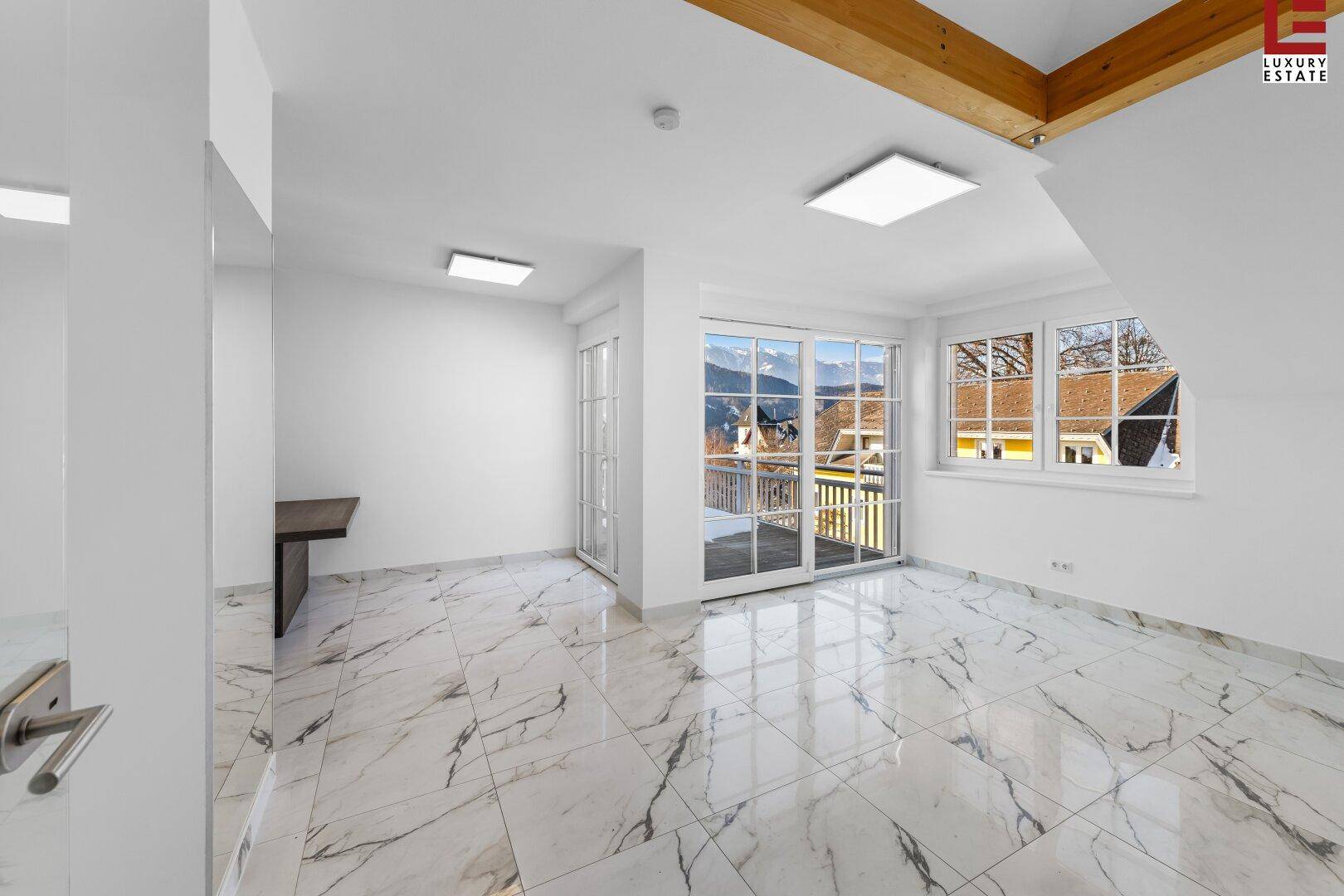 Heller Wohnbereich mit Marmorfliesen, Holzbalken und Zugang zu einem Balkon mit Bergblick.