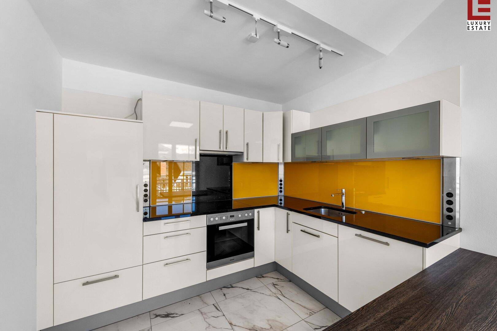 Moderne Einbauküche mit weißen Hochglanzfronten, gelber Rückwand und schwarzen Arbeitsplatten.