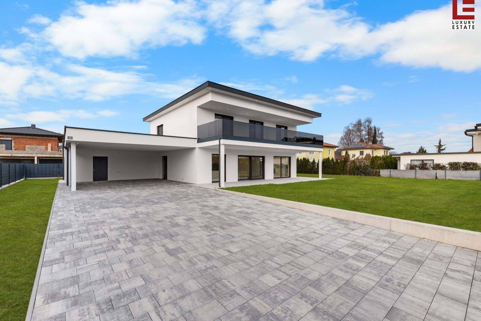 Elegante moderne Villa mit Flachdach, großem Garten und Carport an einem sonnigen Tag.