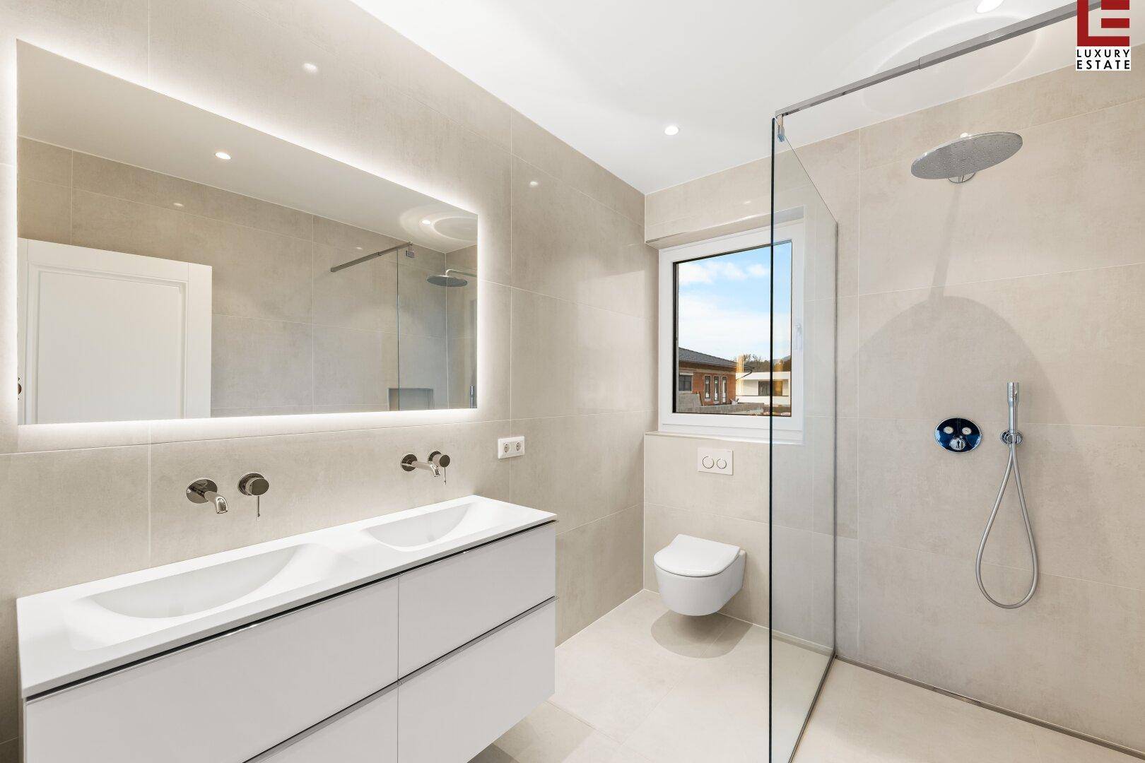 Modernes Badezimmer mit Doppelwaschbecken, großer Dusche und Fenster für Tageslicht.