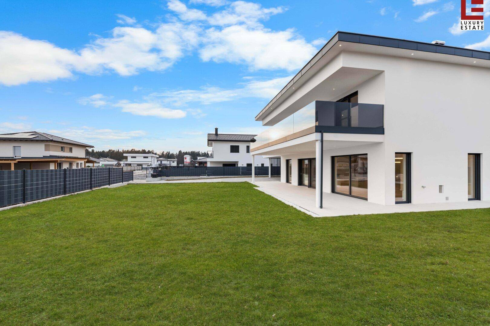 Rückansicht der modernen Villa mit großem Rasen und Zugang zur Terrasse.