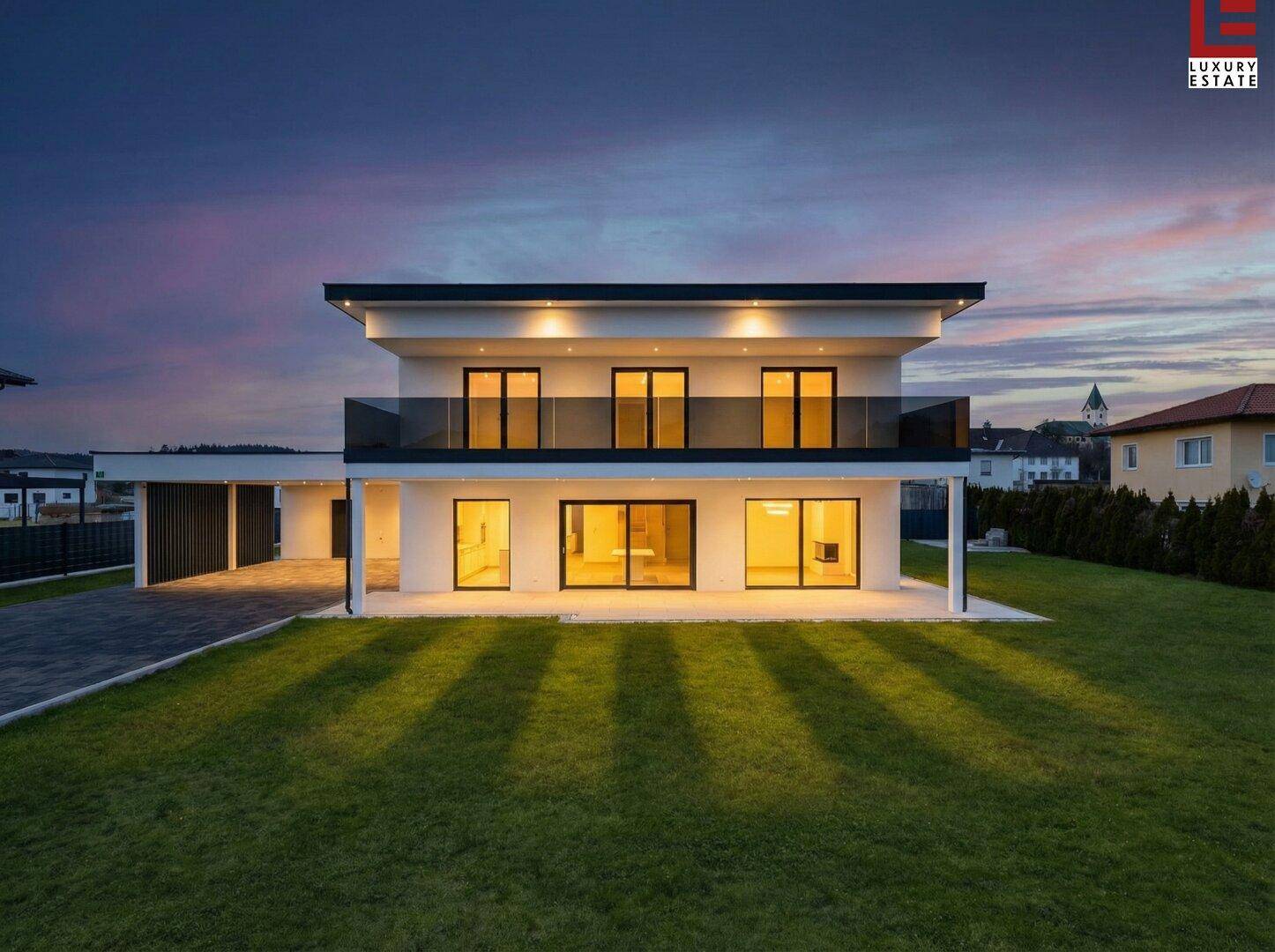 Moderne Villa bei Sonnenuntergang mit beleuchtetem Garten und eleganter Architektur.