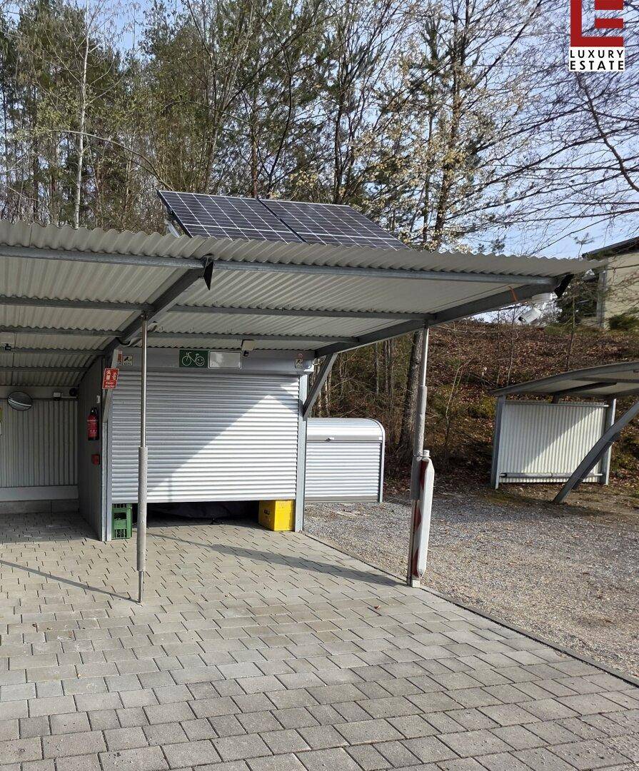 Überdachter Stellplatz mit Photovoltaikanlage und Fahrradabstellraum in grüner Umgebung.