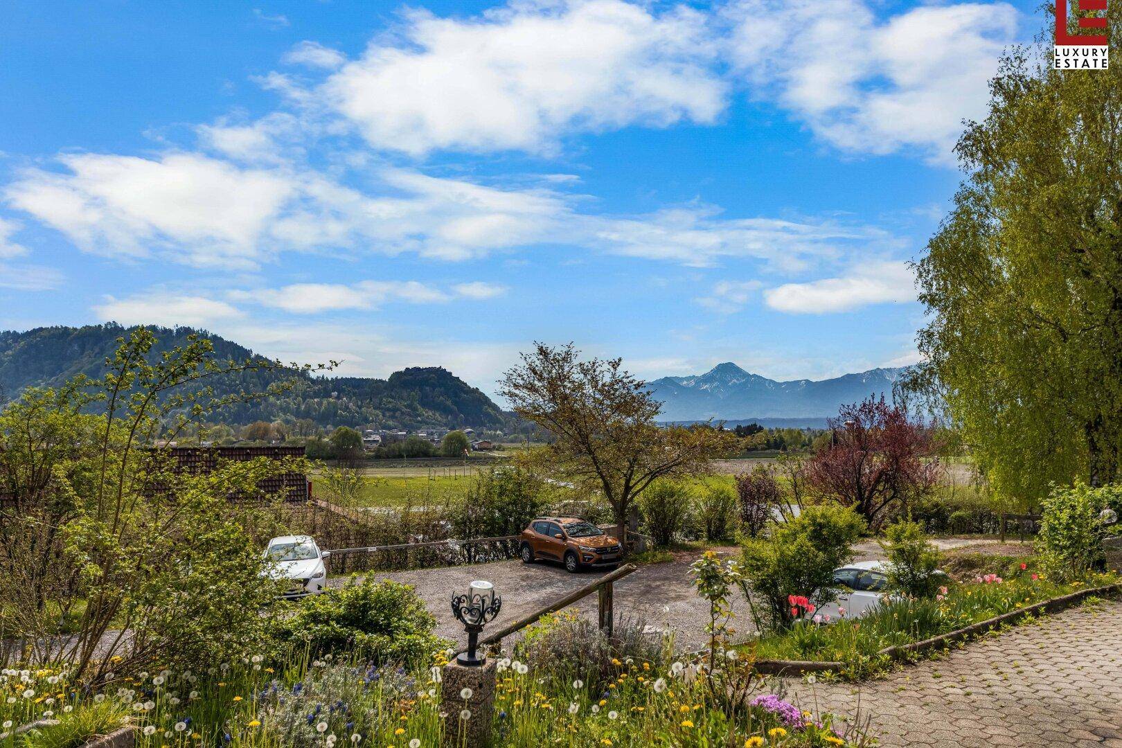 Außenbereich mit Parkplätzen, Blumenbeeten und einem weiten Blick auf die umliegende Berglandschaft.
