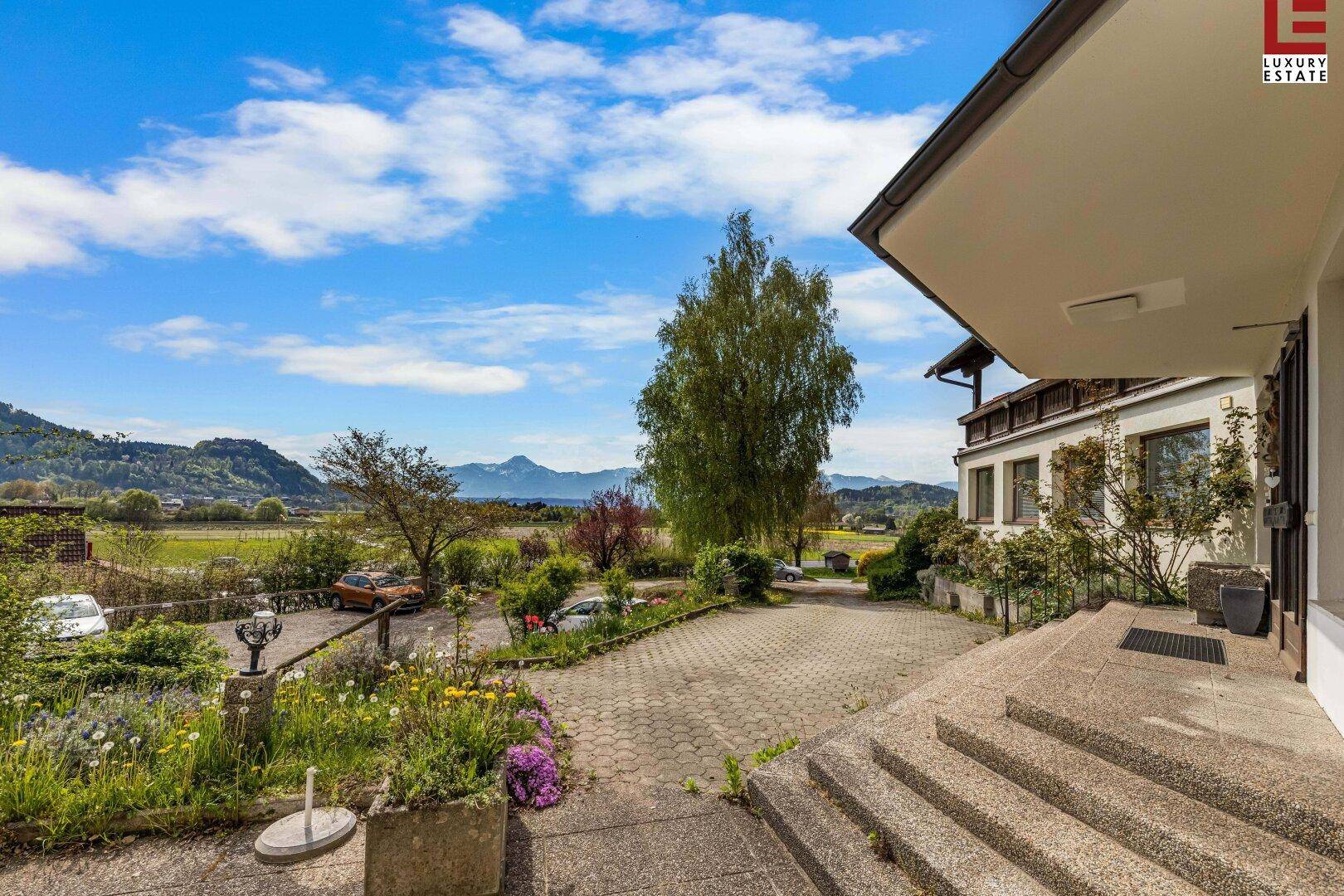 Eingangsbereich des Gebäudes mit Treppe, gepflastertem Vorplatz und weitem Blick auf die Landschaft.