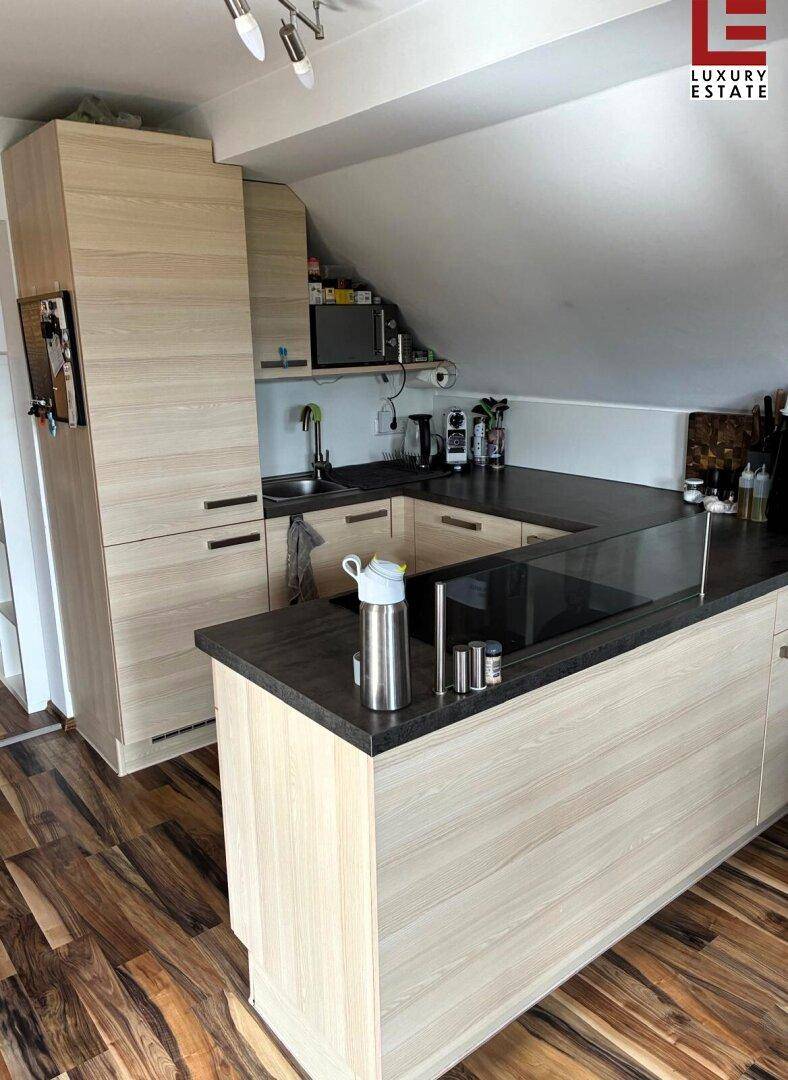 Moderne Küchenzeile in einem Dachgeschoss mit Holzoptik-Schränken und dunkler Arbeitsplatte.