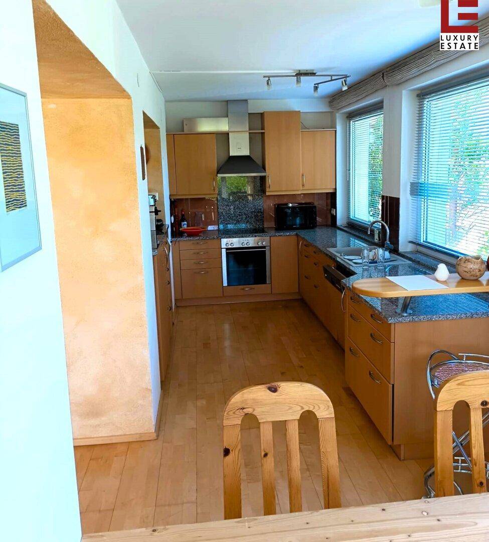 Geräumige Küche mit Holzschränken, Granitarbeitsplatten und Blick in den Garten durch große Fenster.