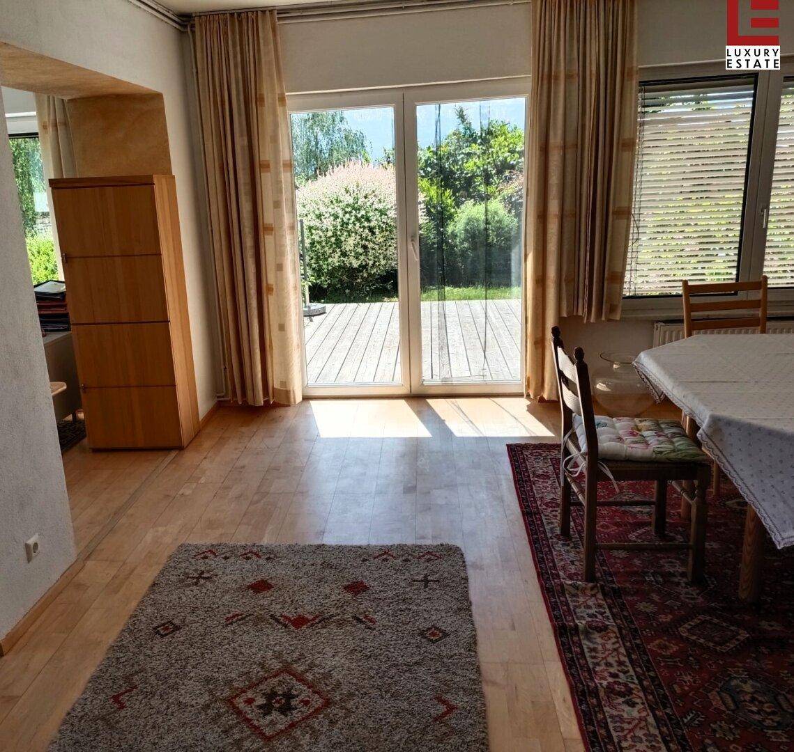 Heller Essbereich mit Holzboden, großem Fenster und Zugang zu einer Holzterrasse im Grünen.