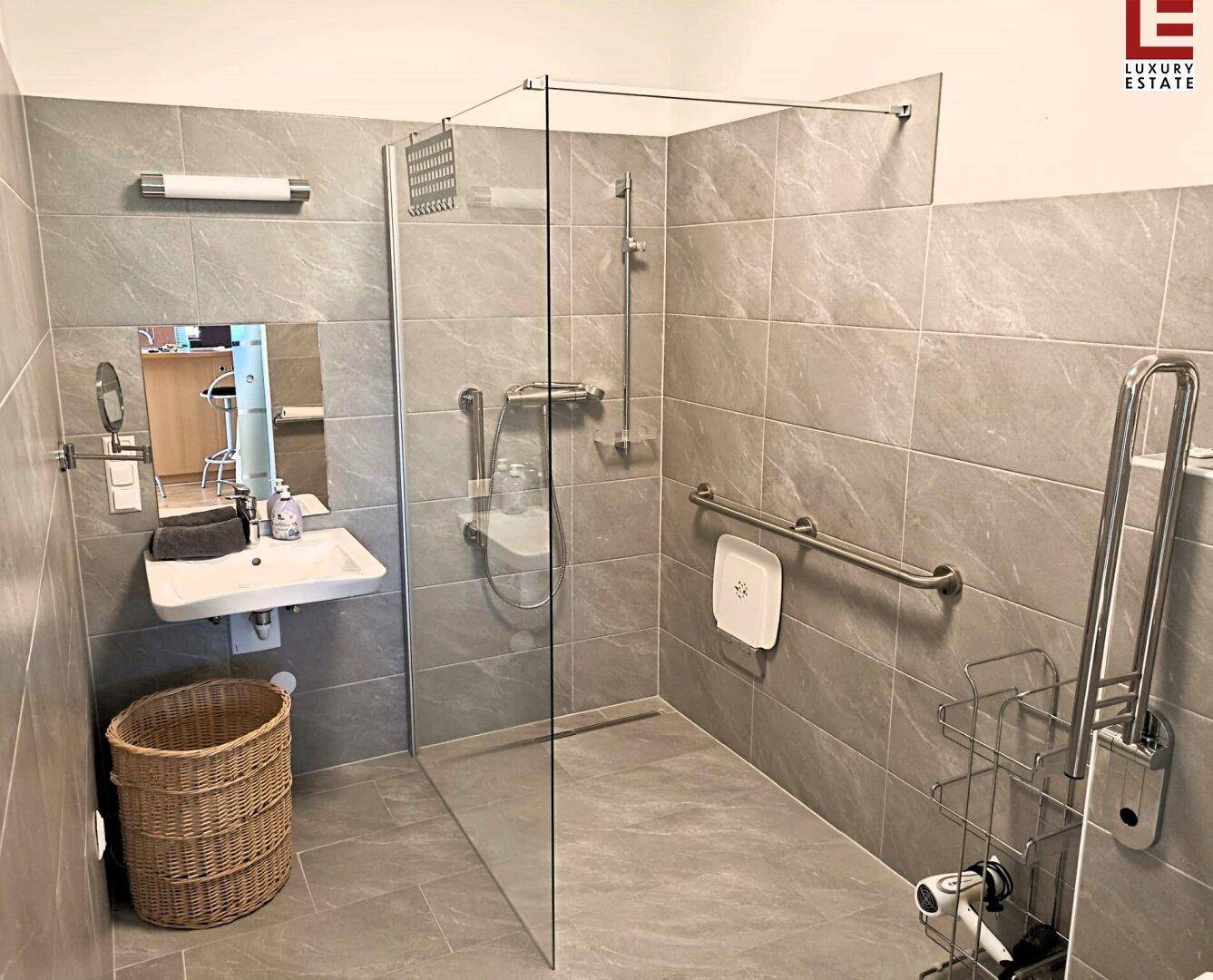 Modernes Badezimmer mit ebenerdiger Dusche, grauen Fliesen und Haltegriffen für Barrierefreiheit.