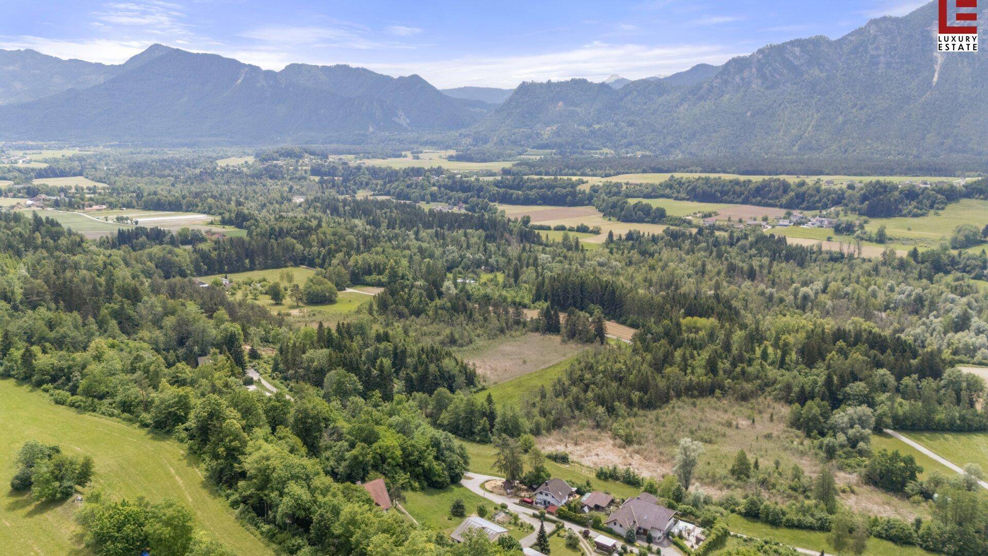 Luftaufnahme eines Baugrundstücks in einer weitläufigen Naturlandschaft mit beeindruckendem Bergpanorama.