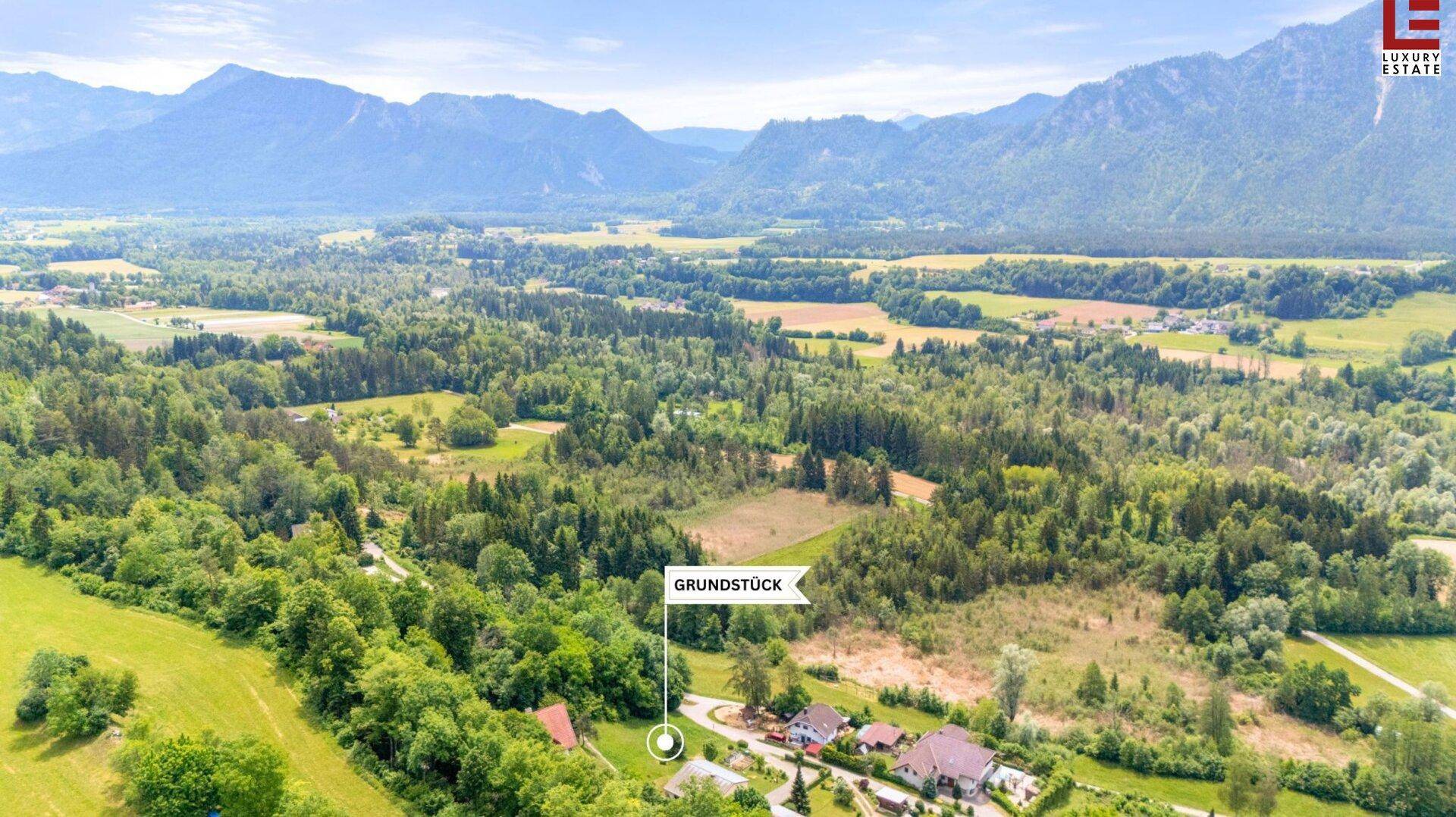 Luftaufnahme eines Baugrundstücks in einer weitläufigen Naturlandschaft mit beeindruckendem Bergpanorama.
