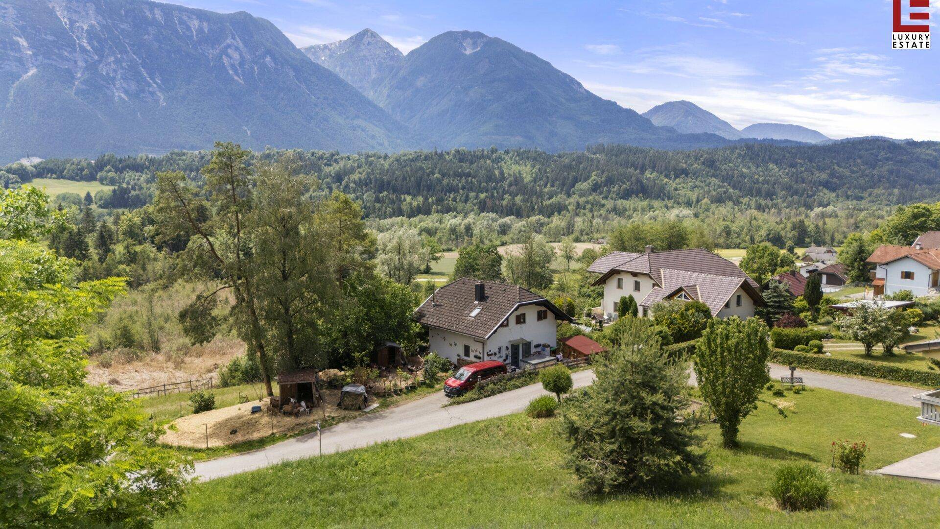 Häuser eingebettet in eine grüne Hügellandschaft mit imposanten Bergen im Hintergrund unter klarem Himmel.