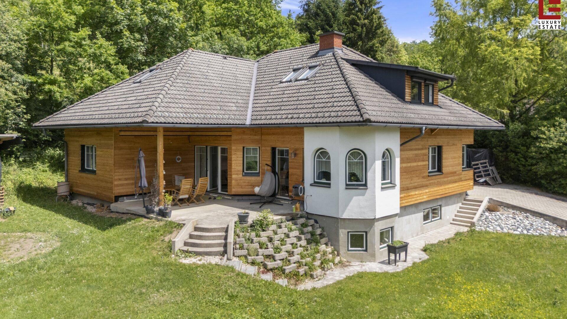 Charmantes Haus mit Holzfassade, großer Terrasse und Blick ins Grüne an einem sonnigen Tag.