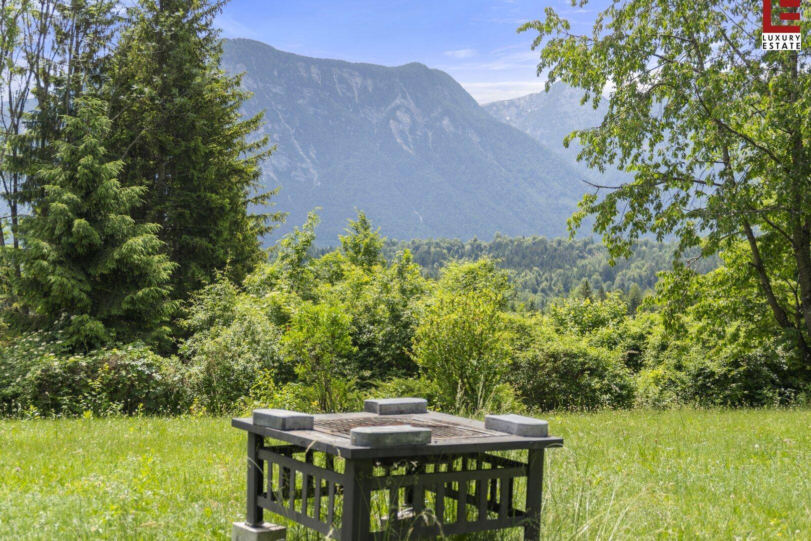 Gartenbereich mit rustikalem Tisch und beeindruckendem Bergblick unter blauem Himmel.
