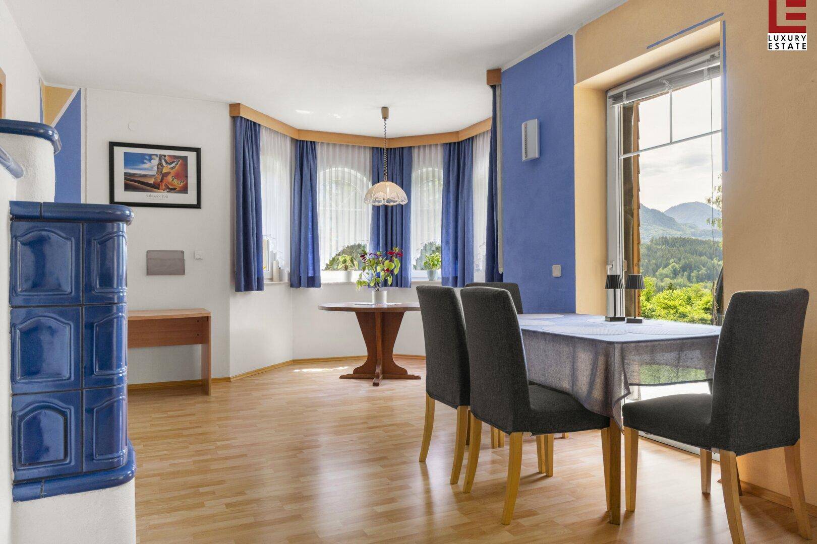 Heller Essbereich mit Holzboden, Kachelofen und großen Fenstern mit Bergblick.