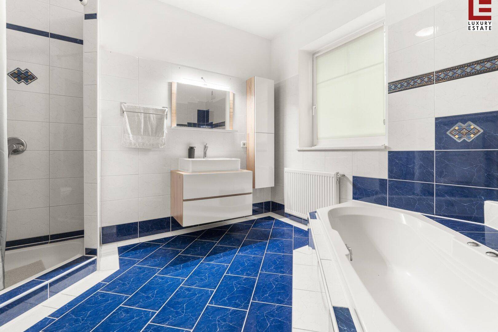 Badezimmer mit blauen und weißen Fliesen, Badewanne und separater Dusche.