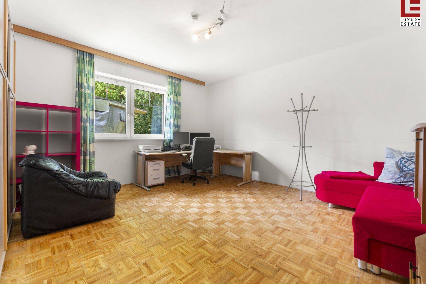 Helles Arbeitszimmer mit Parkettboden, großem Schreibtisch und Blick ins Grüne.