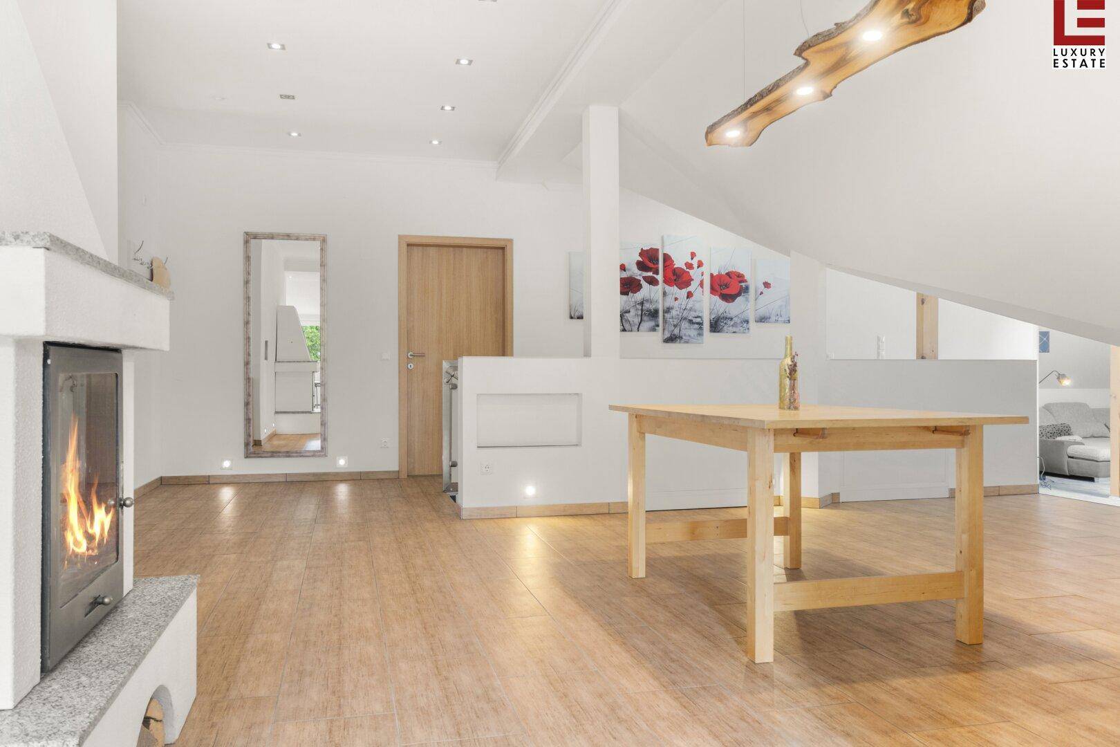 Offener Wohnbereich im Dachgeschoss mit Kamin, Holzboden und moderner Beleuchtung.