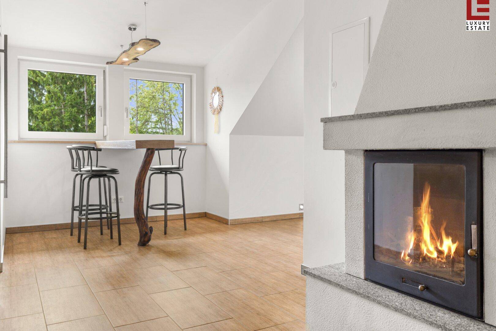 Gemütlicher Barbereich mit Kamin, Holzboden und Blick ins Grüne durch große Fenster.