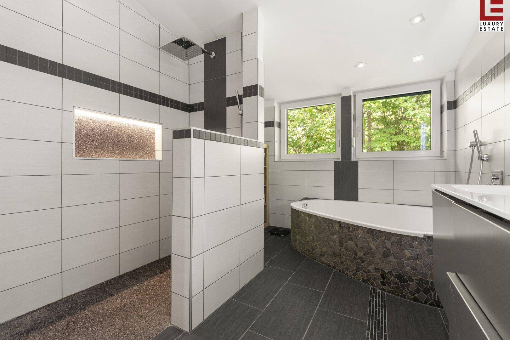 Modernes Badezimmer mit weißen und grauen Fliesen, Badewanne und großer begehbarer Dusche.