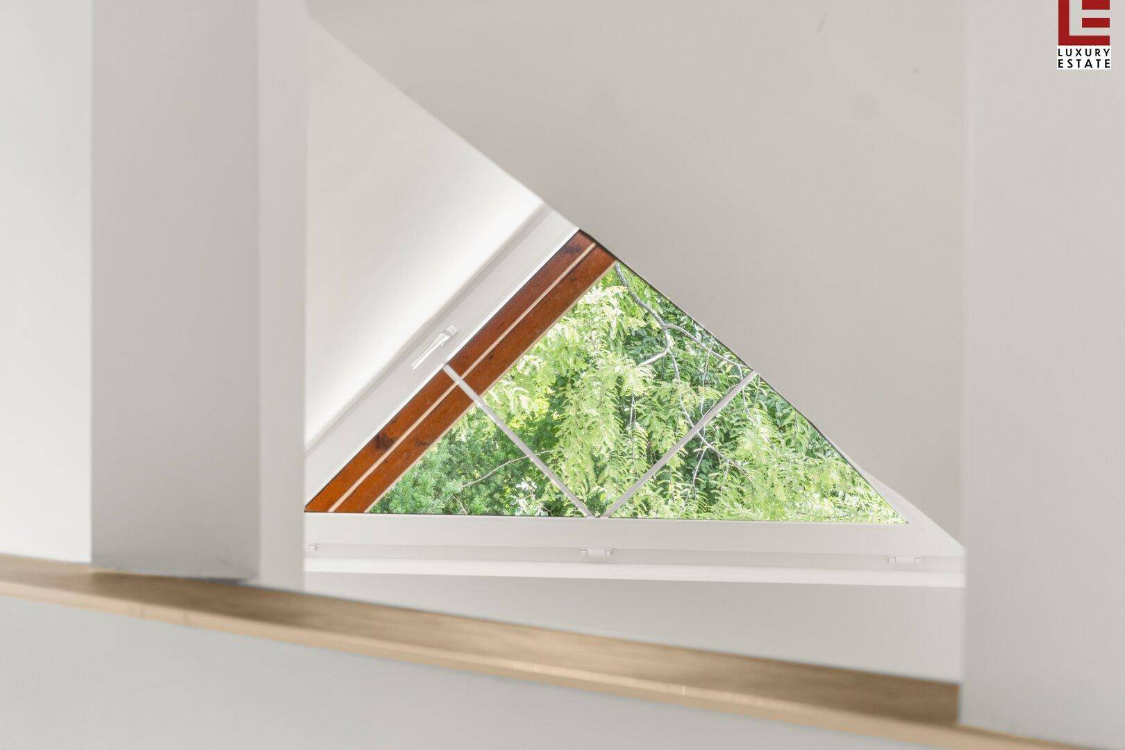 Dreieckiges Fenster in einem Dachgeschossraum mit Blick ins Grüne und Holzelementen.